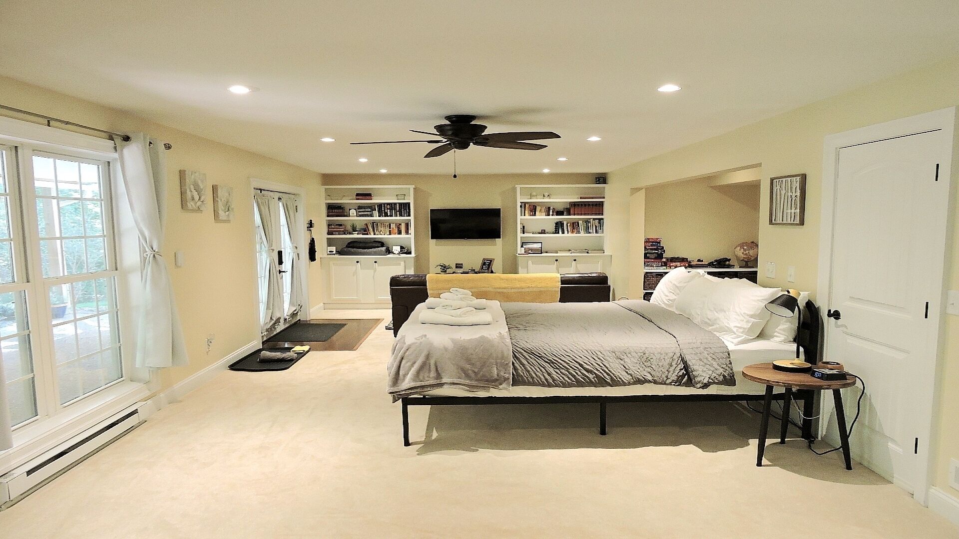 A bedroom with a bed, bedside table, and a ceiling fan. There are bookshelves and a TV in the room.