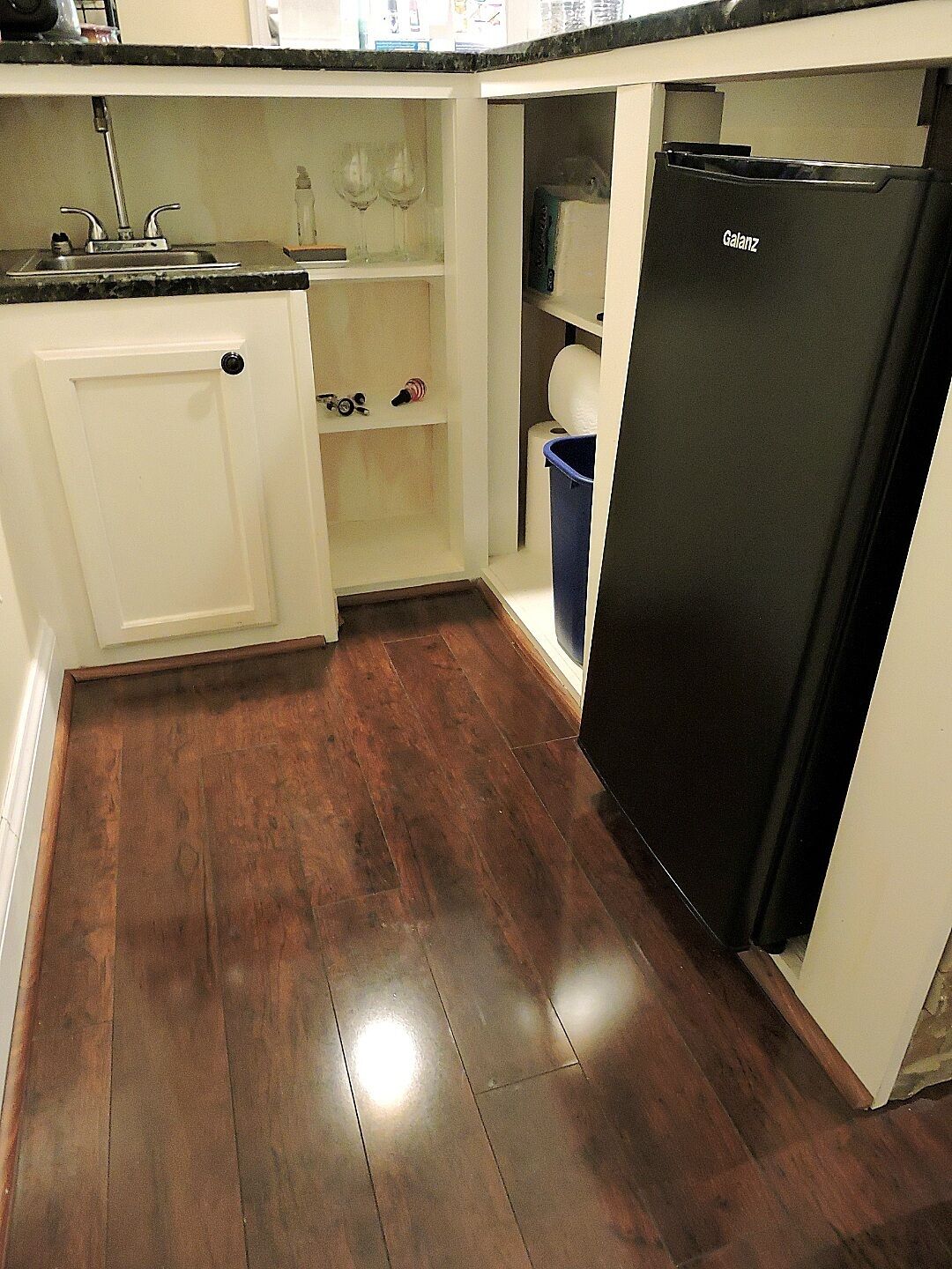 A compact kitchen with a black refrigerator, white cabinetry, and a wooden floor.