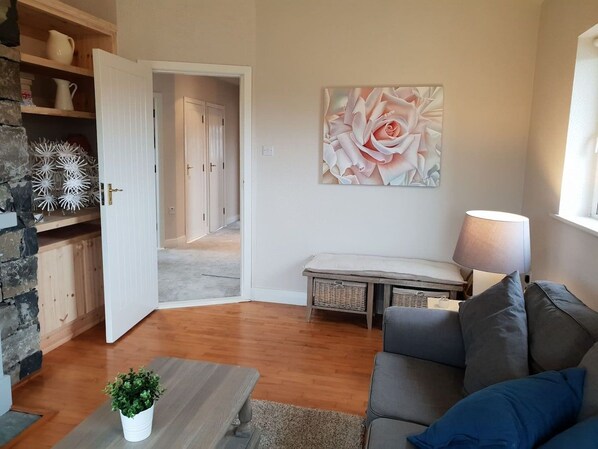 A living room with a sofa, a coffee table, a lamp, a painting, and a door leading to another room.
