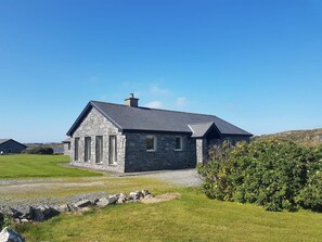 A stone house with a sloped roof, a gravel driveway, and a well-maintained lawn.