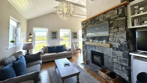 Amplia sala de estar con chimenea de piedra, un televisor grande montado en la pared y una zona de estar acogedora con sofá y sillones.
