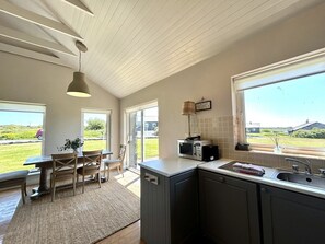 A modern kitchen with a dining area, large windows, and a view of the outdoors.