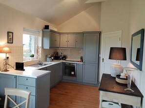 A compact kitchen with grey cabinets, a central island, a built-in oven, and a small dining area with a chair.