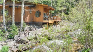 A wooden cabin with a deck, surrounded by trees and a rocky stream. - Cabin on Clear Creek: A Hobbit’s Retreat! (Black Hawk)