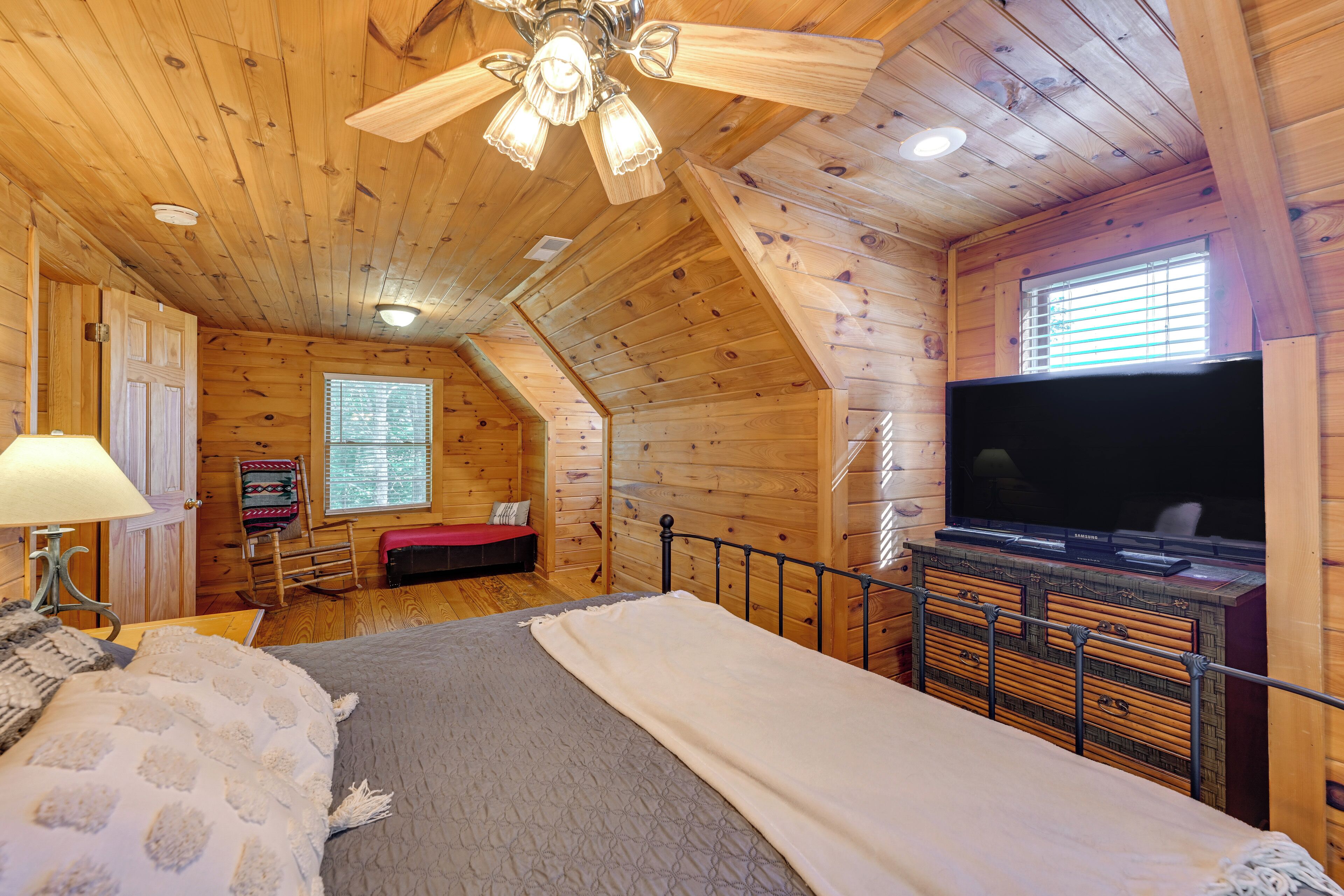 A cozy wooden cabin bedroom with a bed, a television, and a ceiling fan.