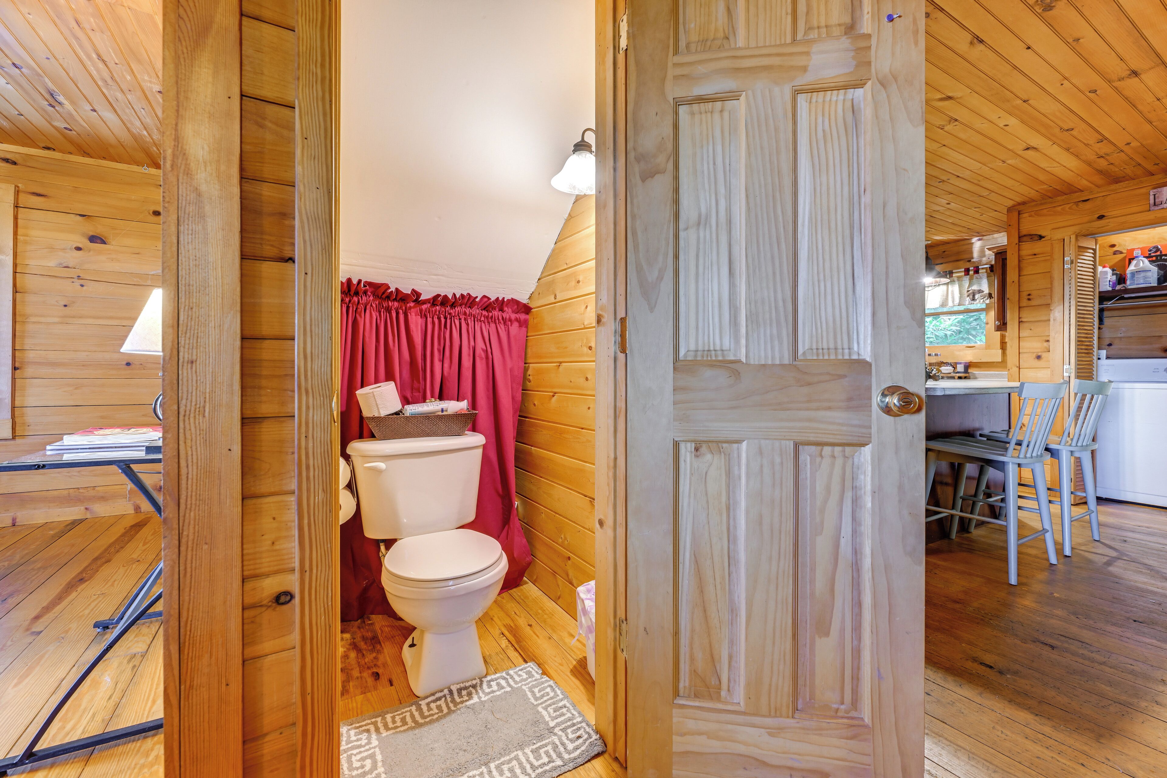 A wooden interior with a wooden door, a white toilet, and a red curtain.