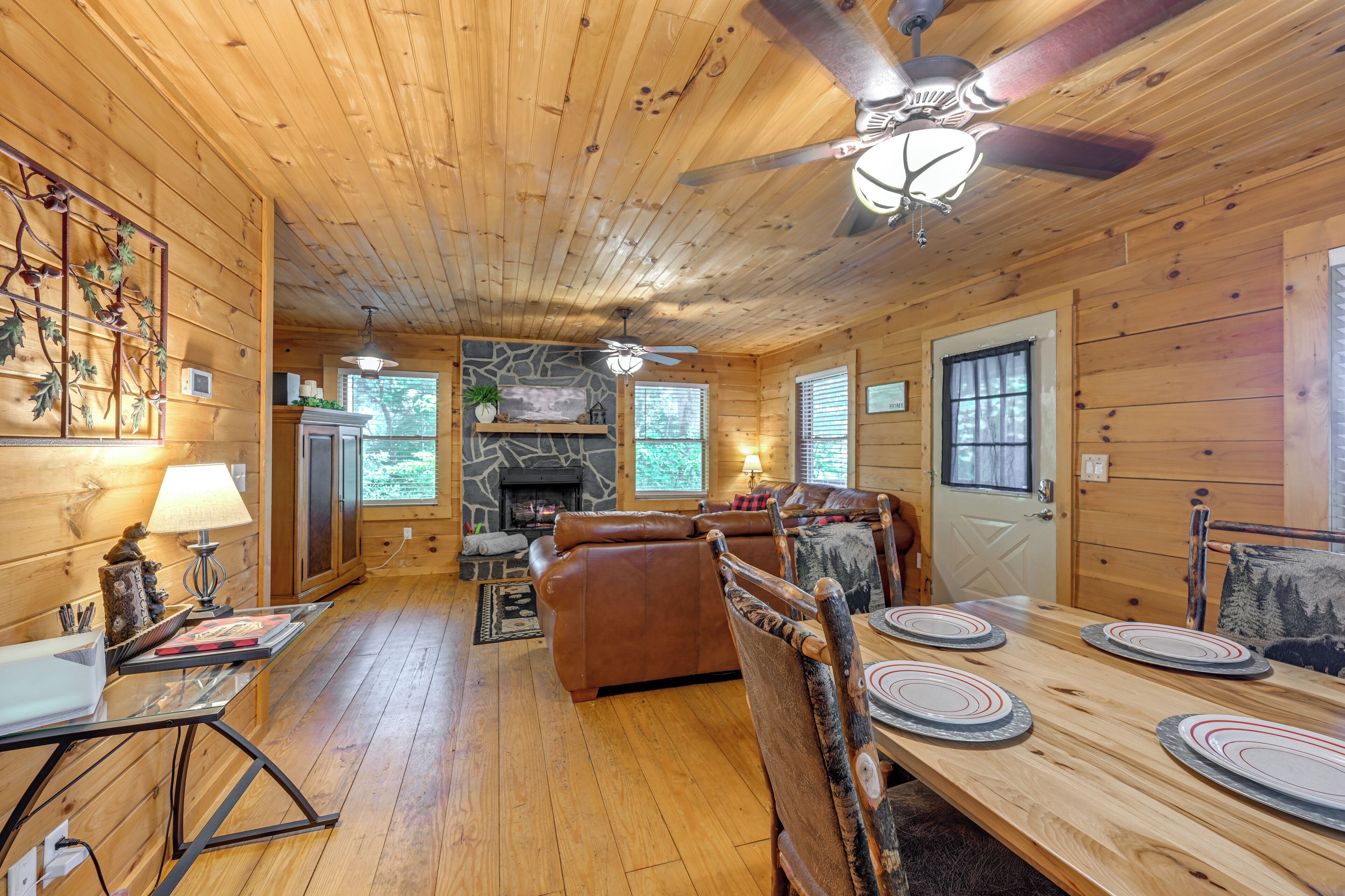 A wooden cabin interior with a dining area, fireplace, and ceiling fans.