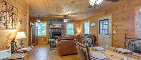 A wooden cabin interior with a dining area, fireplace, and ceiling fans.