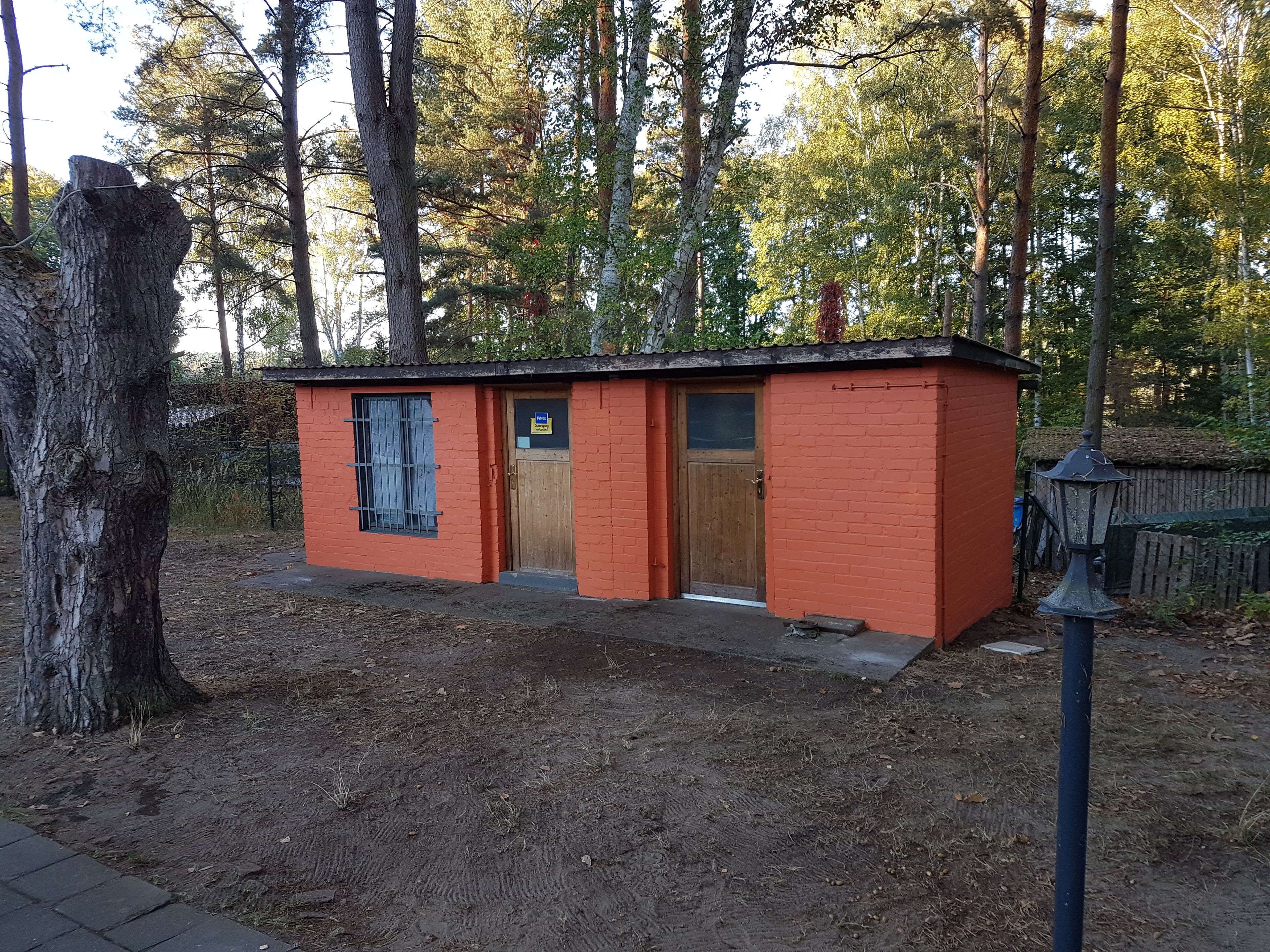 A small, single-story building with a wooden door and a window, surrounded by trees.