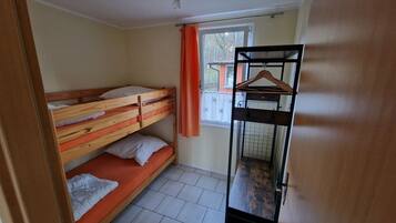 Une chambre de dortoir avec des lits superposés, une fenêtre avec des rideaux, un étagère en métal et un sol carrelé.