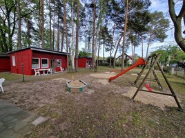 Un parque infantil con tobogán y columpios, rodeado de edificios rojos y árboles.