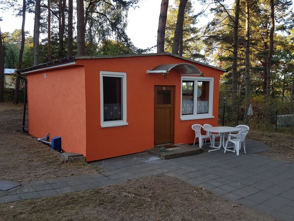A small orange cabin with a door, two windows, and a table with chairs outside.
