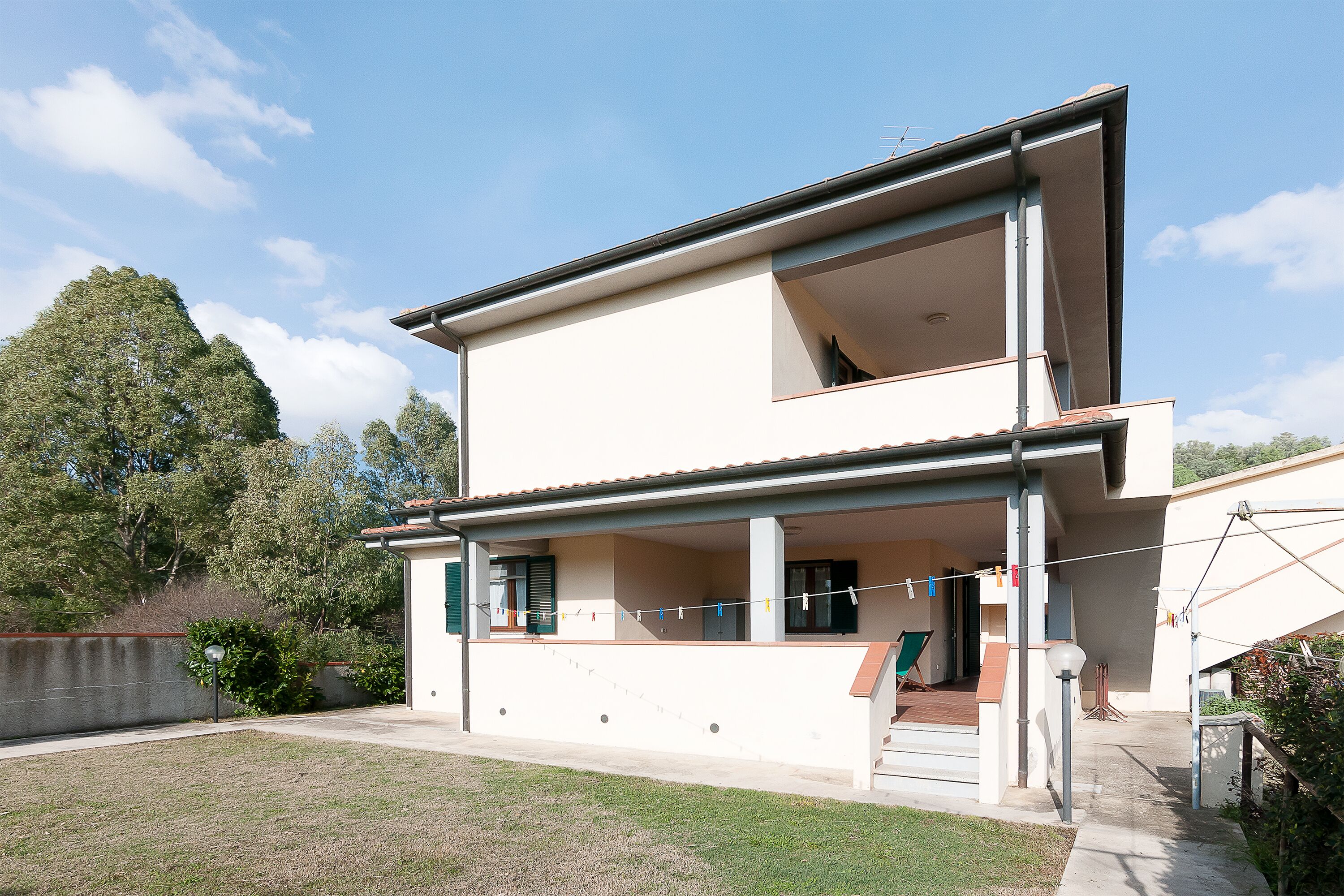 A modern two-story house with a balcony, a small garden, and a clear sky.