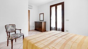 A bedroom with a bed, a wooden dresser, a chair, and a mirror. - Just 500 m from the sandy beach - Primula 2 (Marina di Campo)