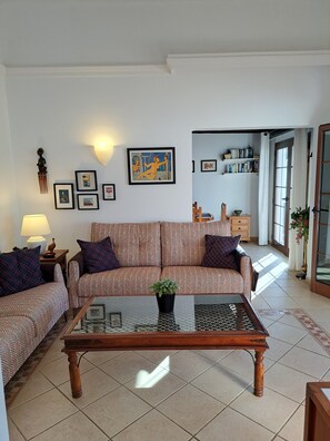 Ein Wohnzimmer mit einer Sofagarnitur, einem Couchtisch, Wandbildern und einem Bücherregal.