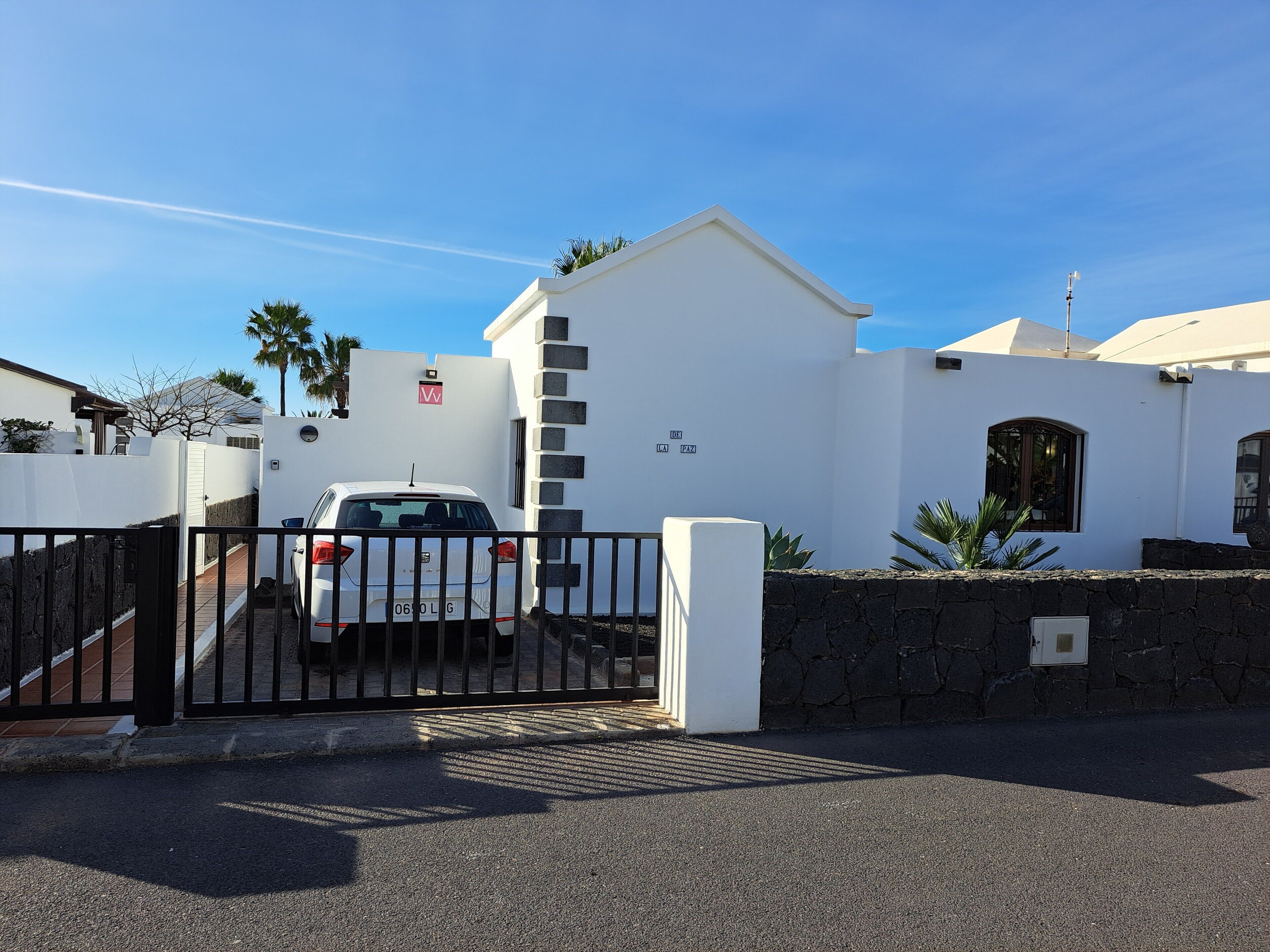 Ein begrenzter Eingang zu einem Gebäude mit weißer Fassade, ein geparktes Auto davor und ein klarer, blauer Himmel.