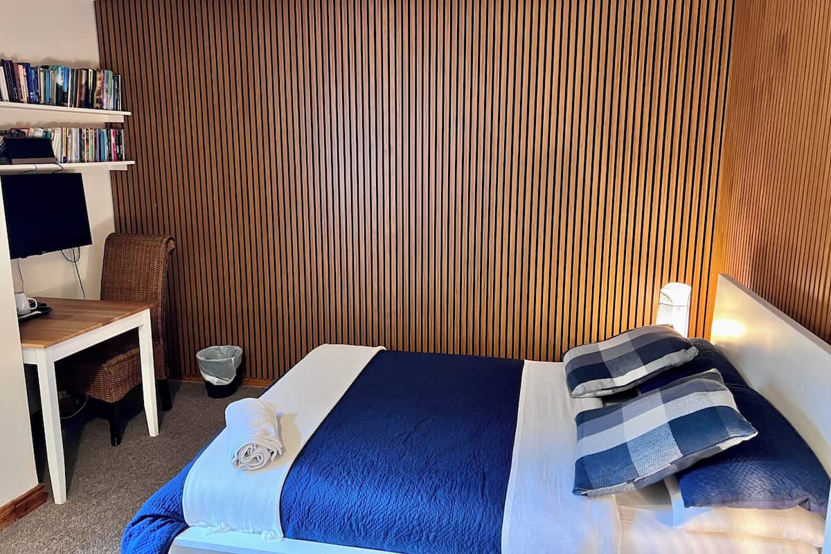 A neatly arranged hotel room with a bed, a small desk, a television, and a bookshelf.