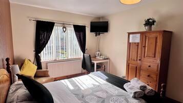 A hotel room with a bed, a desk, a television, a cabinet, and a window with curtains.