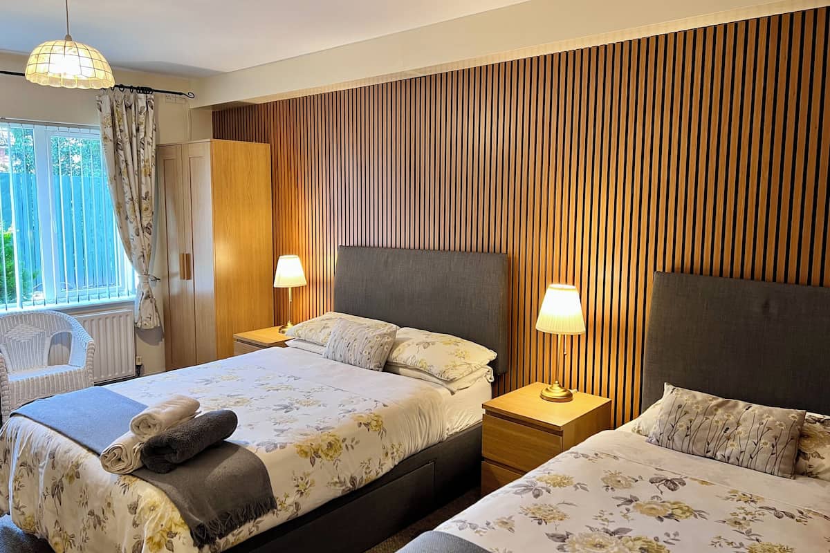 A hotel room with two beds, wooden paneling on the walls, a window with curtains, and two bedside lamps.