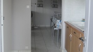Un couloir avec un sol carrelé, un coin repas avec une table et des chaises, un espace cuisine avec un évier et des placards, et un espace buanderie avec une machine à laver et un étendoir.
