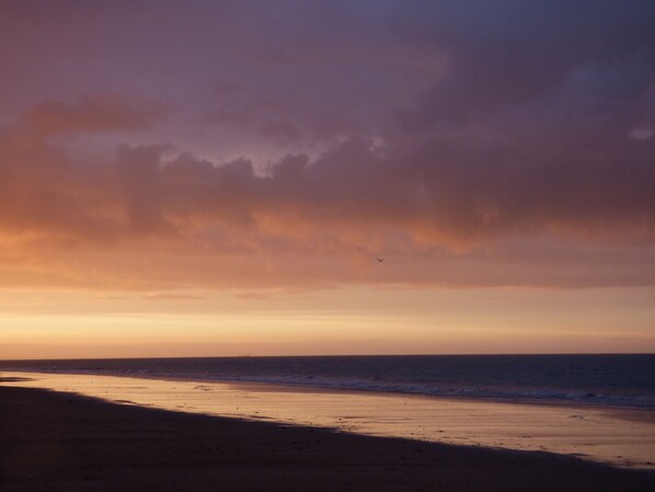 Een strand bij zonsondergang met een heldere lucht en een rustige zee.