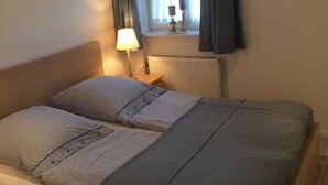Una cama individual con estructura de madera, una mesita de noche con lámpara y una ventana con cortinas.