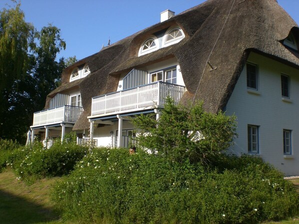 Une grande maison blanche, dotée d’un toit de chaume et de nombreux balcons.