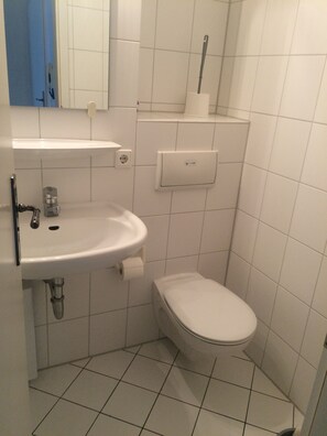 Une petite salle de bain propre, avec un lavabo, des toilettes et un miroir, le tout de couleur blanche.