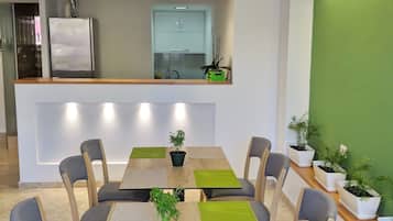 Un comedor moderno con mesas y sillas de madera, manteles individuales verdes y plantas en macetas.