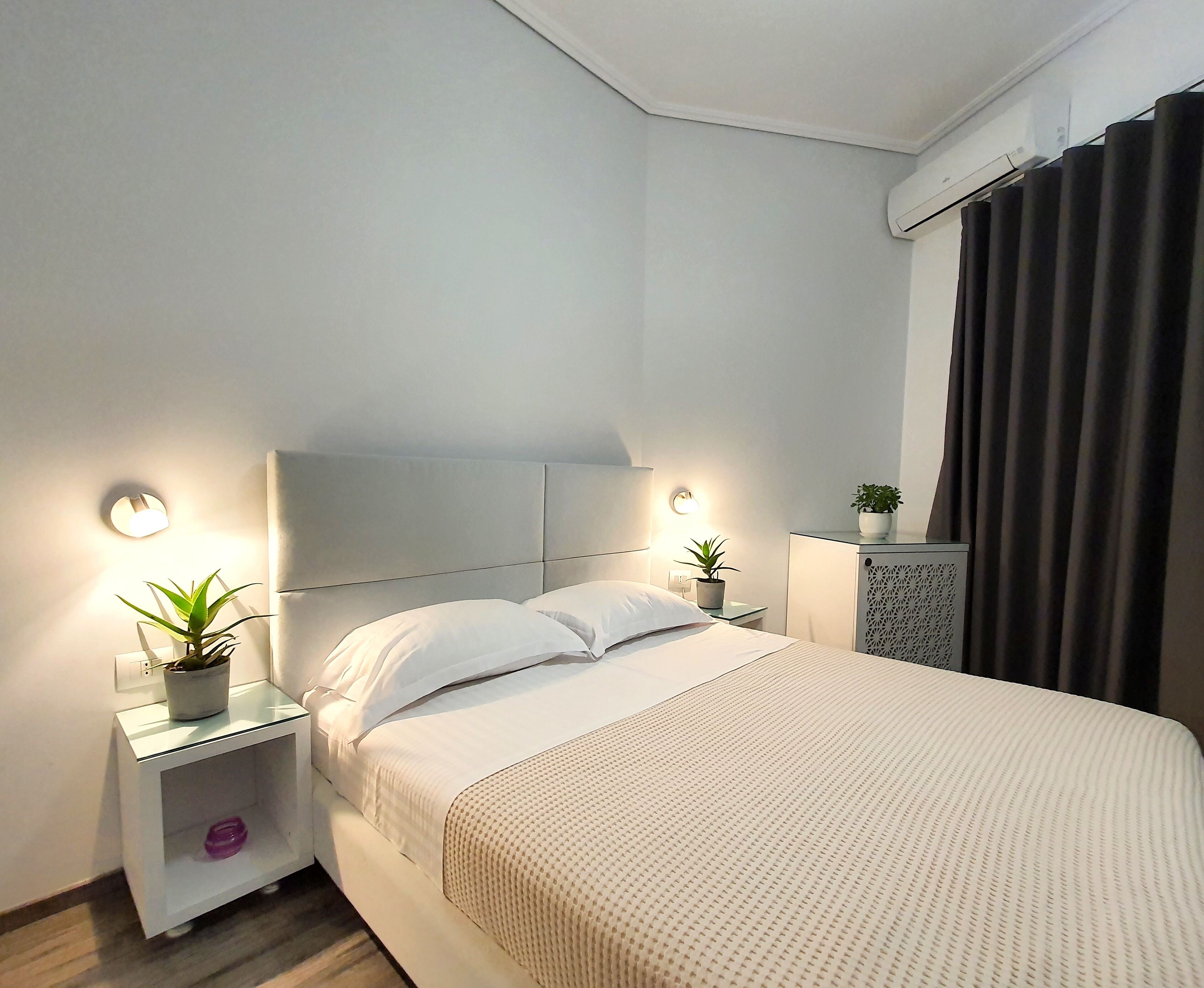 A modern bedroom with a bed, bedside tables, and a potted plant.