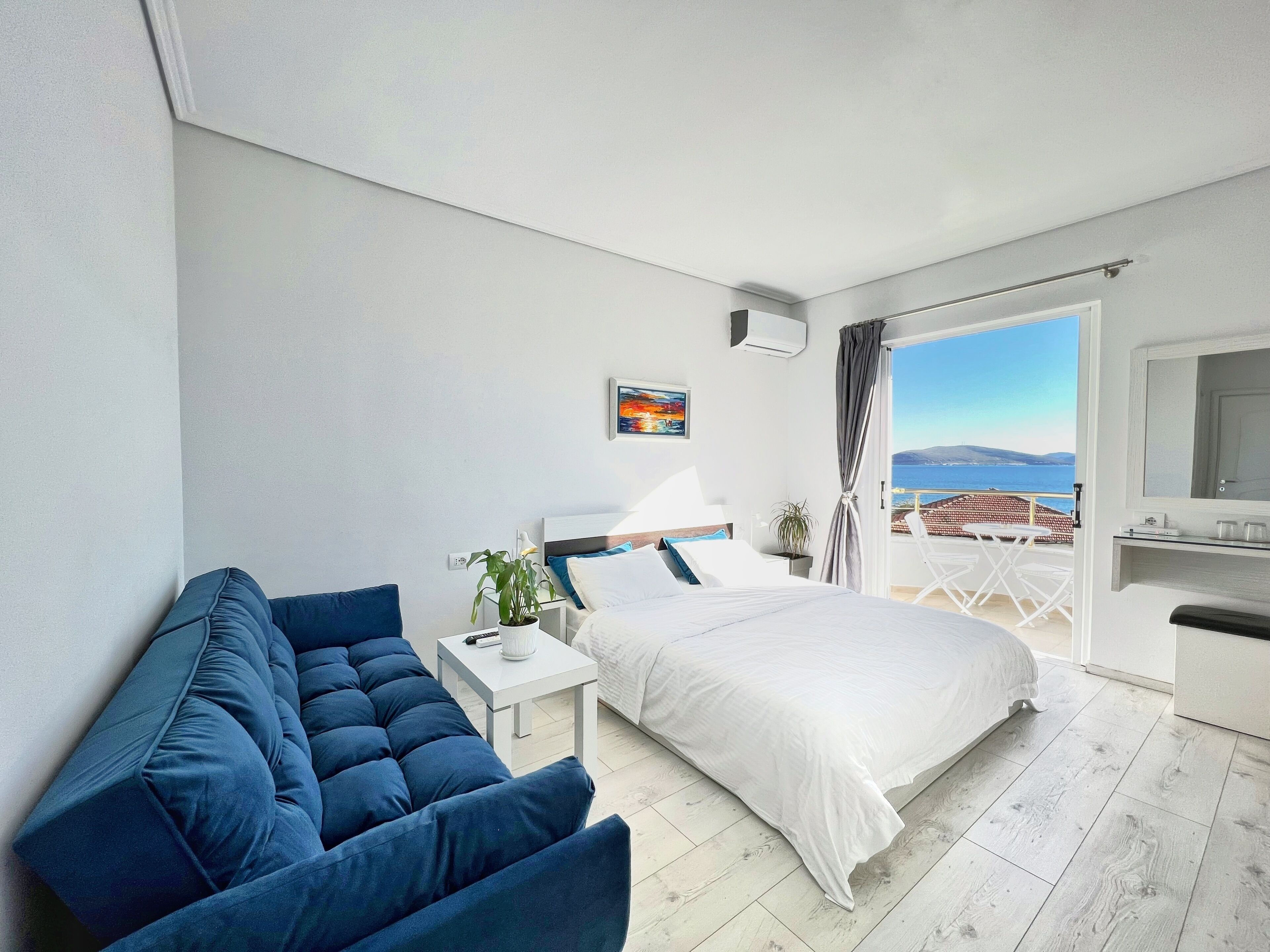 Una habitació d'hotel moderna amb un llit, un sofà, una taula petita i un balcó amb vista al mar.
