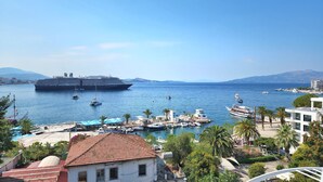 A coastal marina with a large cruise ship docked, smaller boats, and a variety of buildings including a white building with a red roof. - Hotel JoAn (Sarandë)