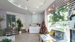 A hotel lobby with a reception desk, a Christmas tree, and a seating area with a yellow ottoman. - Hotel JoAn (Sarandë)