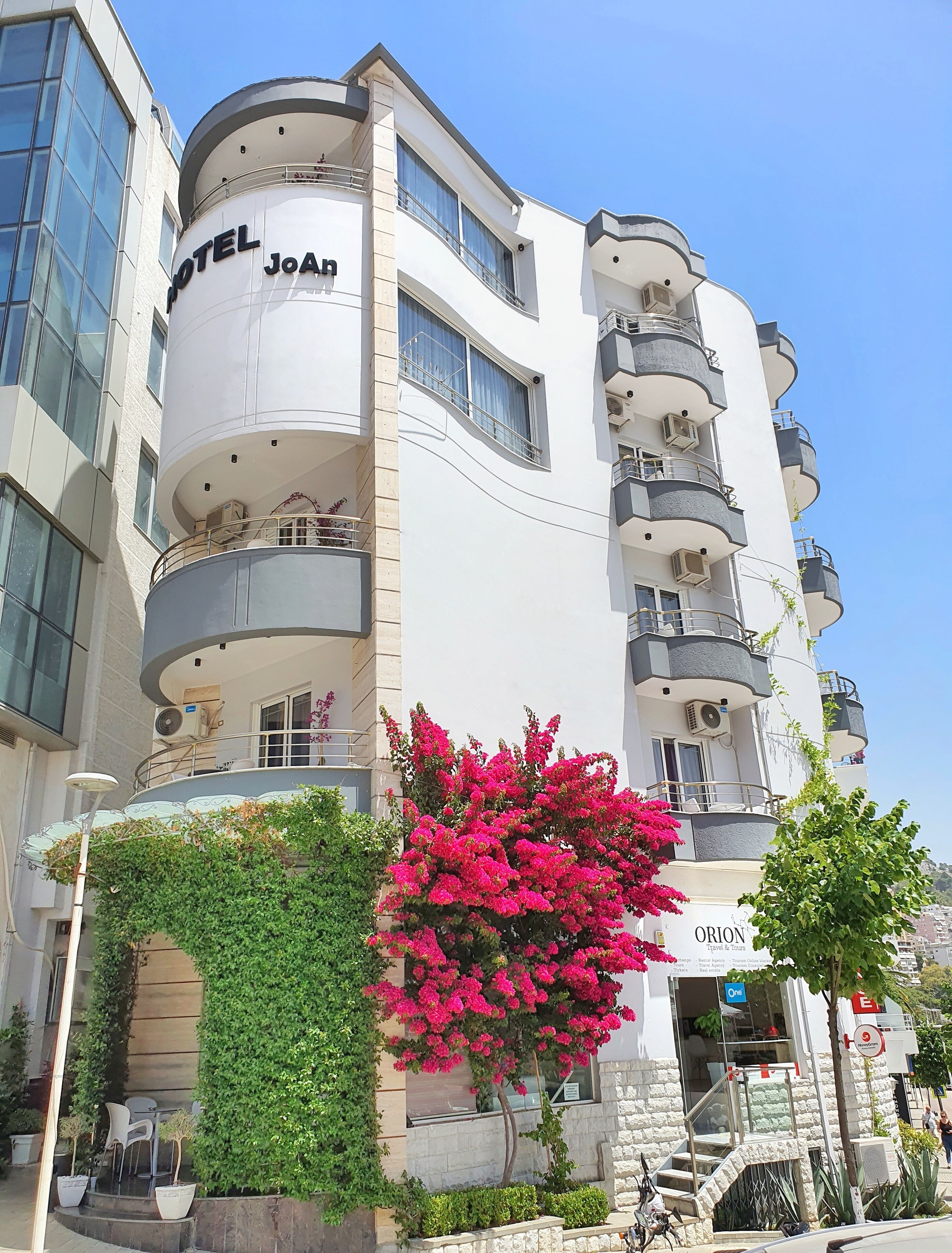 Un hotel de varios pisos con balcones, una entrada visible y un letrero que dice 'ORION Travel & Tours'.
