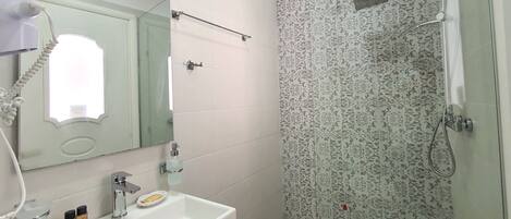 A bathroom with a white sink, a mirror, a handheld showerhead, and a patterned shower wall.