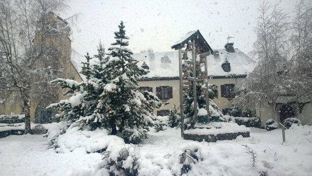 Un patio cubierto de nieve, con un árbol nevado, una torre de campanas y un edificio con múltiples ventanas.