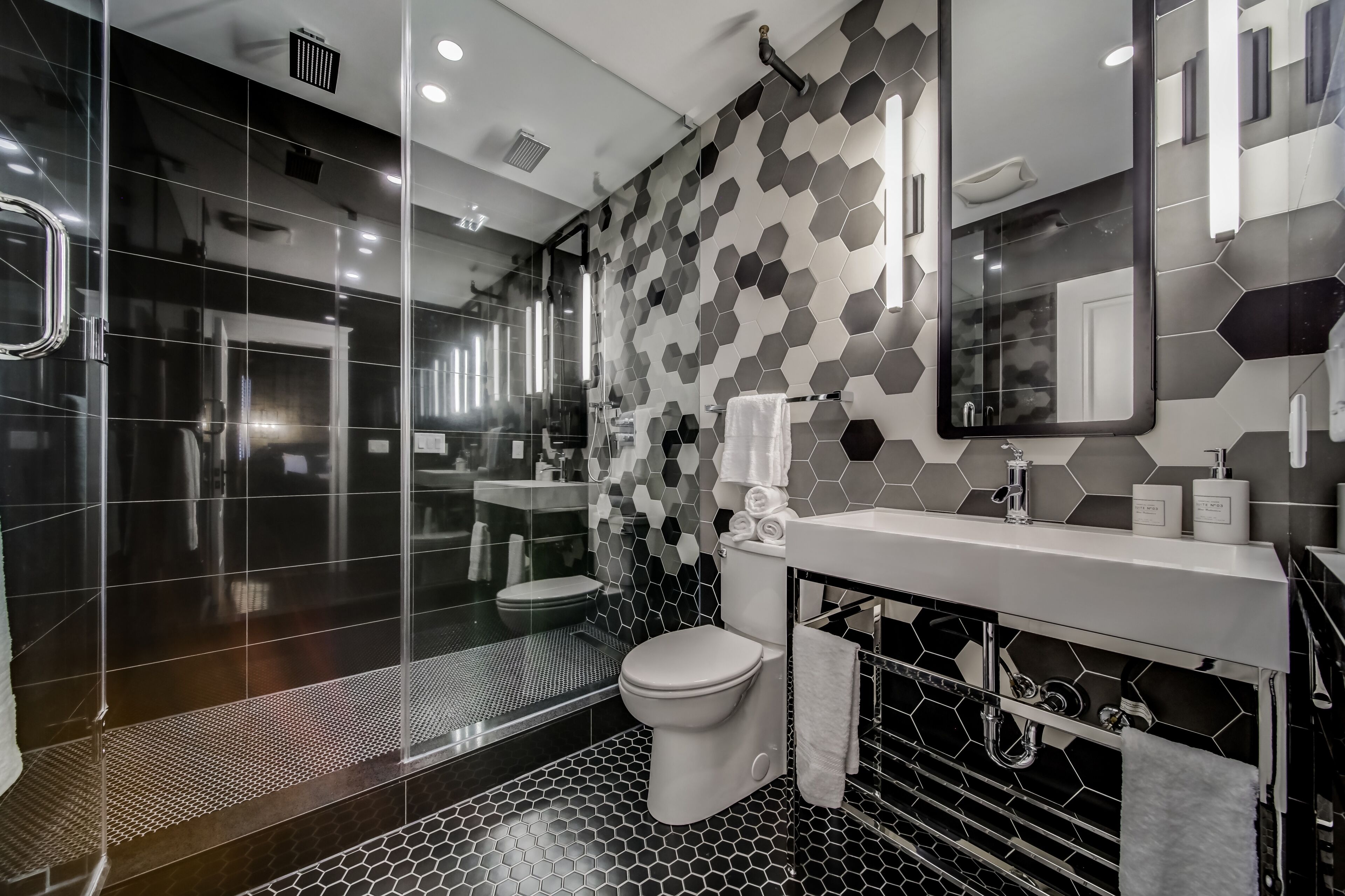 Un baño moderno con ducha de vidrio, inodoro blanco y lavamanos con espejo.