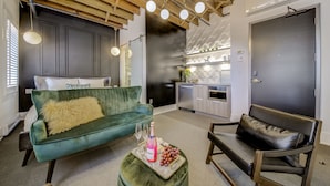 A modern living room with a green velvet sofa, a black leather chair, and a small ottoman with a bottle and glasses. - The Westlake (Toronto)