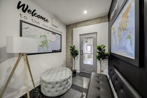 A modern lobby with a welcome sign, a map, a large globe, a round ottoman, and a black leather bench. - The Westlake (Toronto)