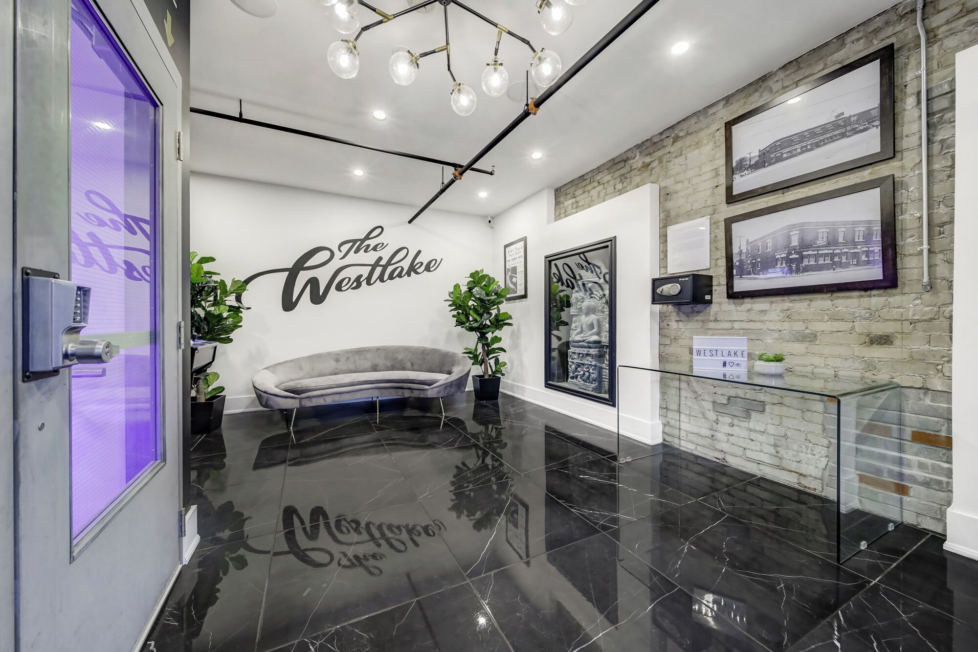 A modern lobby with a sofa, potted plants, a sign reading 'The Westlake,' and framed pictures on the walls.