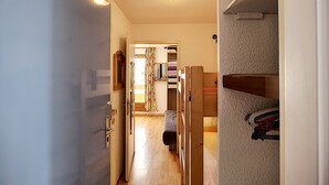 A narrow hallway with wooden flooring, a door on the left, and a closet with shelves on the right.