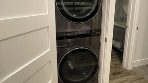Une petite buanderie moderne, dotée de deux machines à laver et de deux sèche-linge à chargement frontal superposés, de murs blancs et d’un plancher en bois.