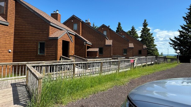 Une rangée de cabanes en bois avec des escaliers extérieurs, une allée gravillonnée et une voiture garée.