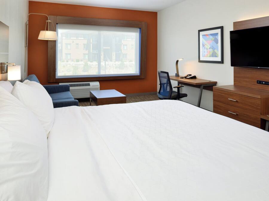 Camera d'albergo con un letto grande, una scrivania, una sedia, una TV e una finestra con vista sugli edifici.