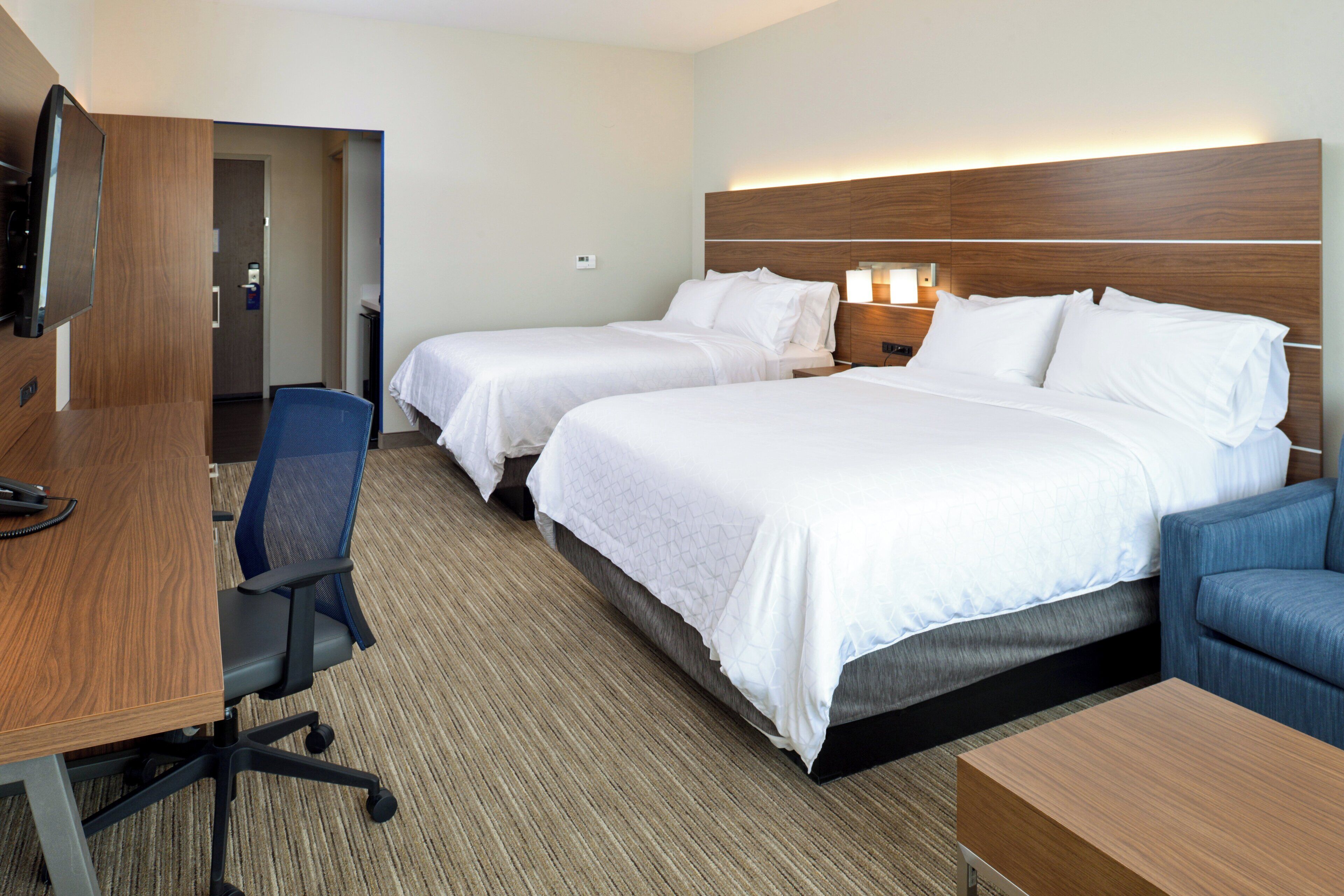 A hotel room with two beds, a desk, a chair, and a TV.