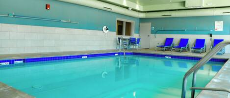 Una piscina con azulejos azules, una barandilla de seguridad y sillas azules a un lado.