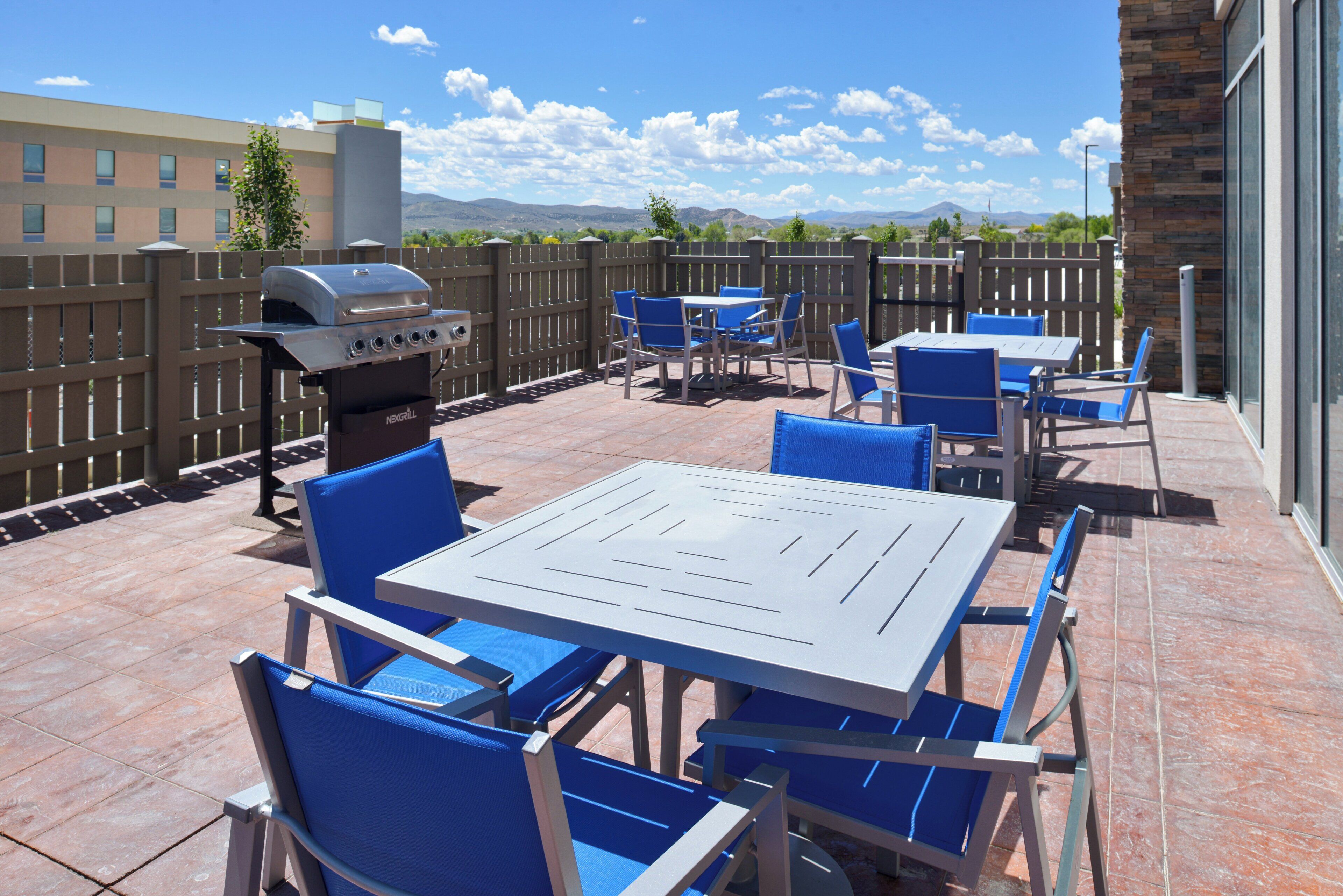 An outdoor patio with a barbecue grill, blue chairs, and a table.