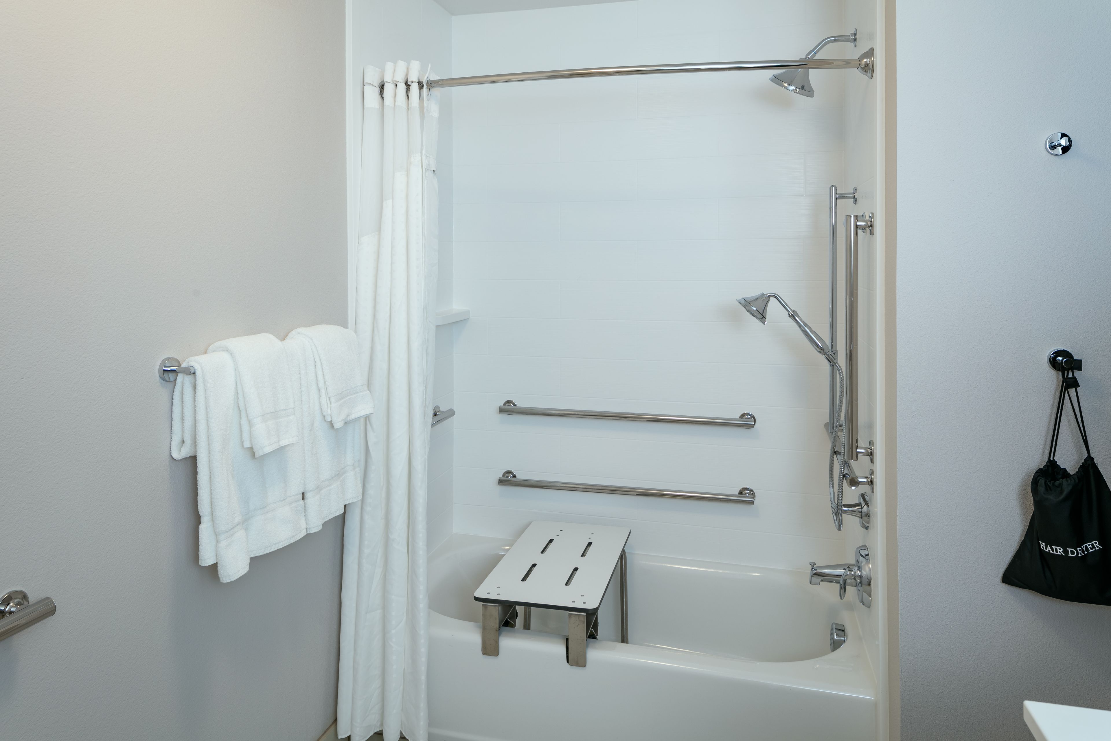 A modern bathroom with a bathtub, grab bars, a towel rack, and a small step stool.