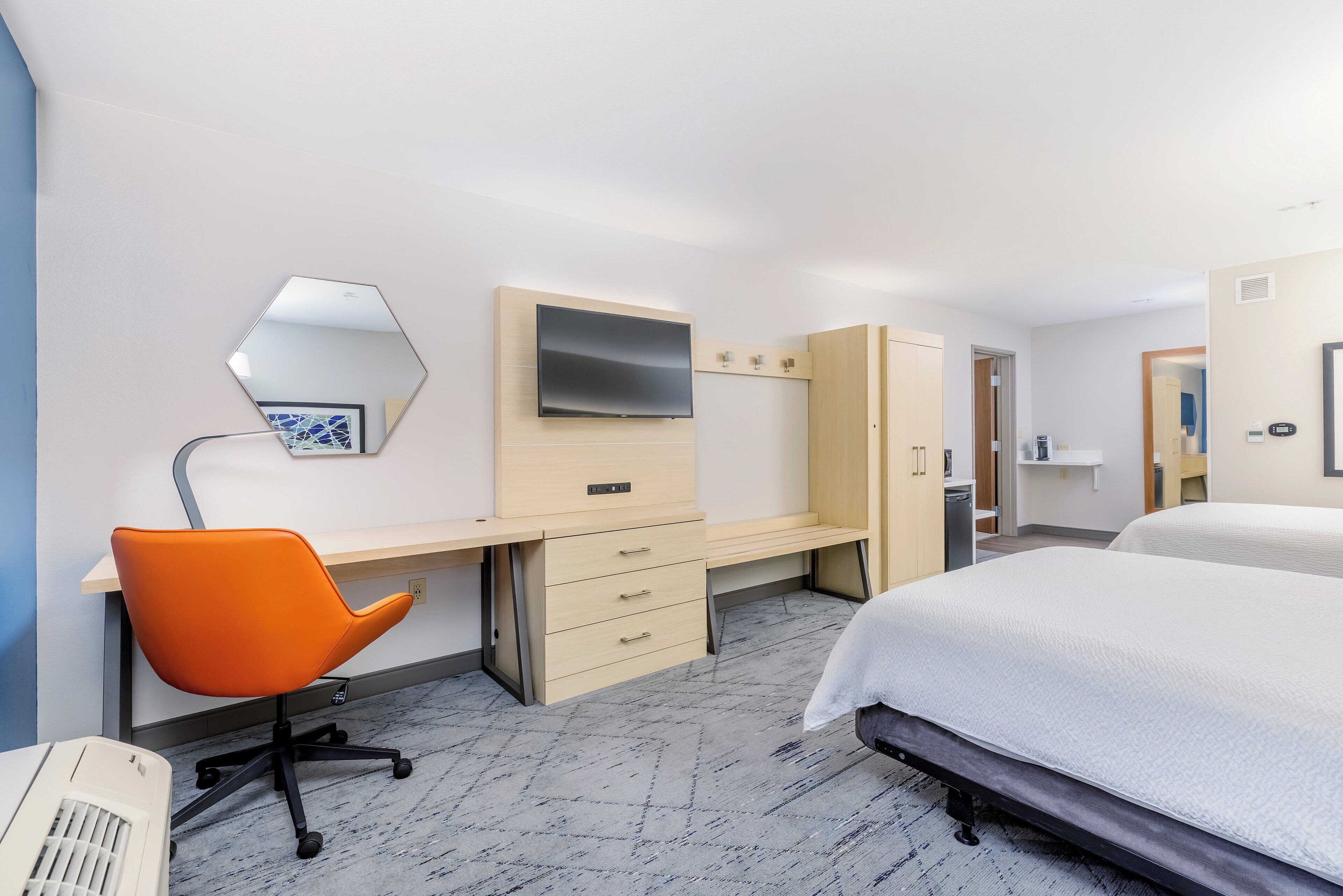 Una habitación de hotel con cama, escritorio con cajones, silla, televisor y armario.