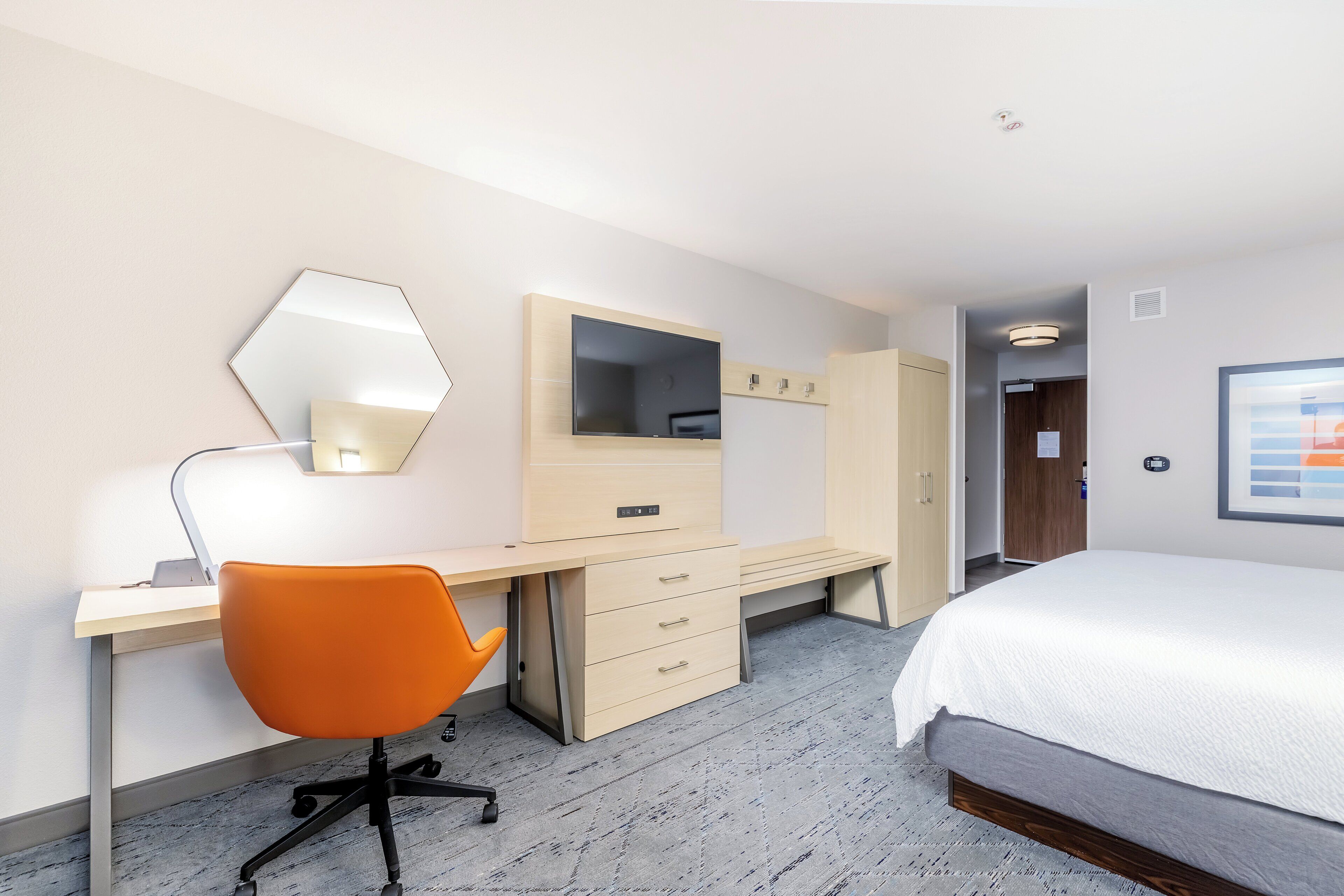 A hotel room with a bed, desk, chair, wardrobe, and a mirror.